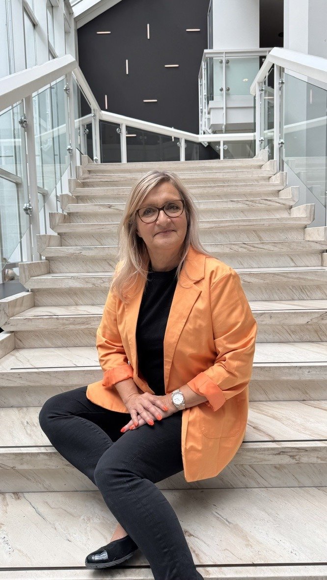 Gabriele Parolini sitzt in einem orangefarbenen Blazer auf einer hellen Treppe.